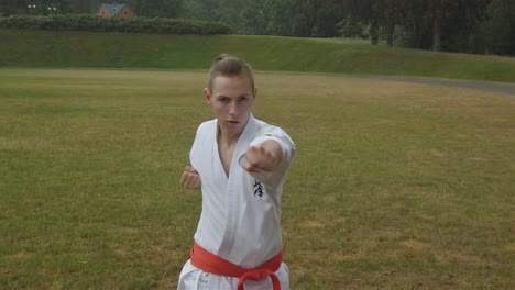 young teenager karate boy practices punches and other fight moves in the rain while moving forward to achieve best shape while being determined