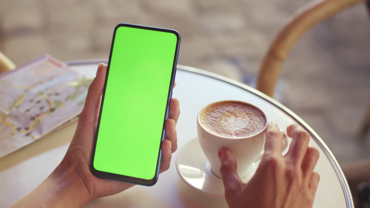 Person holding a green screen smartphone at a cafe table with coffee