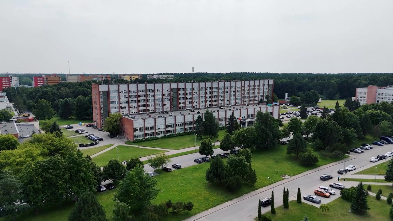 Il lungo blocco di reparti dell'Ospedale Universitario di Klaipėda si erge sopra ampi prati, alberi e strade di accesso in una ripresa aerea statica diurna