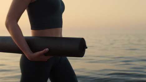 Primer-Plano-Mujer-En-Forma-Caminando-Por-La-Orilla-Del-Mar-Con-Colchoneta-Deportiva.-Mujer-Deportiva-Haciendo-Ejercicio.