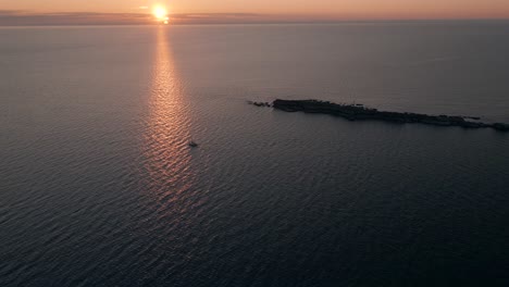 solitary sailboat sailing through the sea near an island during sunset - aerial shot