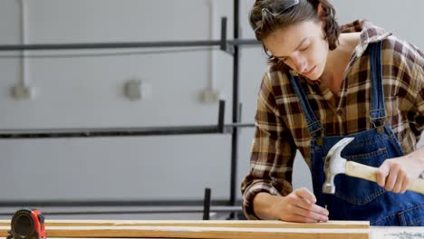 female welder hammering nail on a wooden plank 4k