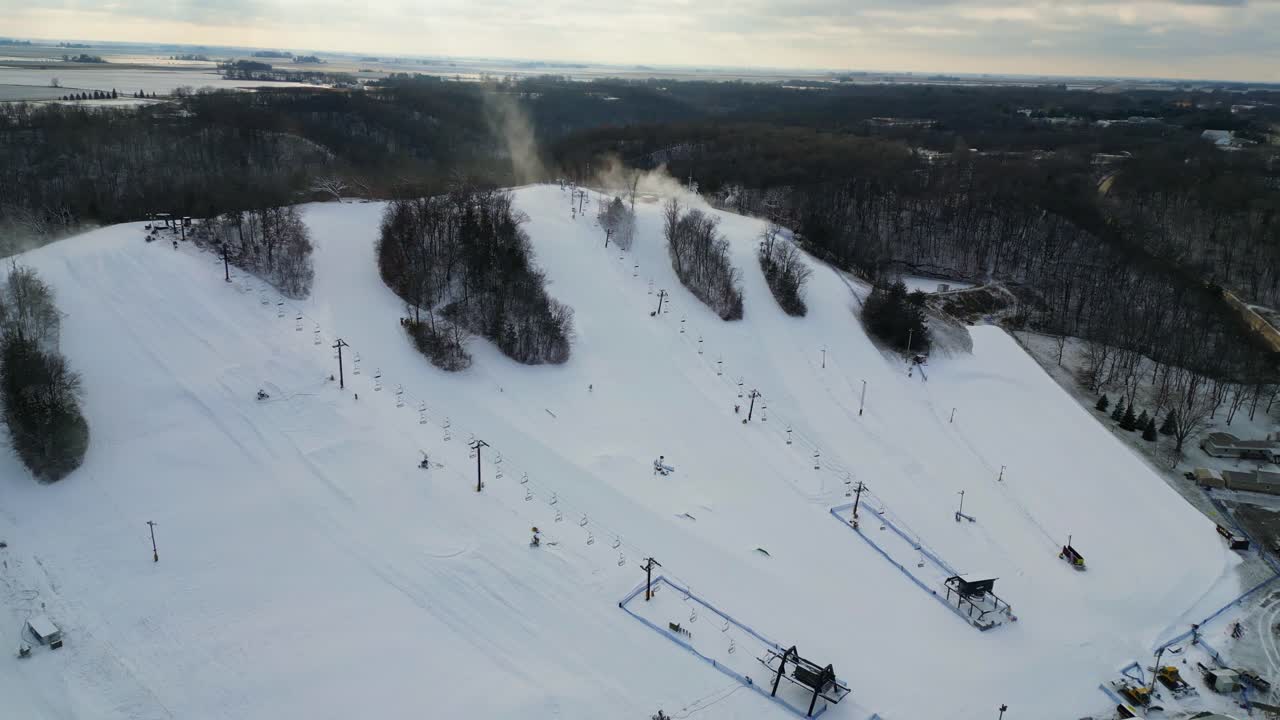 Un'impressionante ripresa aerea cattura una vivace stazione sciistica in una giornata invernale, con numerose piste innevate e cannoni sparaneve attivi che creano neve fresca.