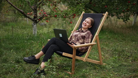 happy attractive lady working remotely on computer sits smiling in the chair. smiling woman closes her laptop and leans back in chair dreamingly.
