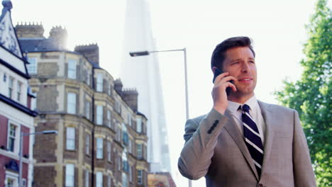 businessman talking on mobile phone walking along city street