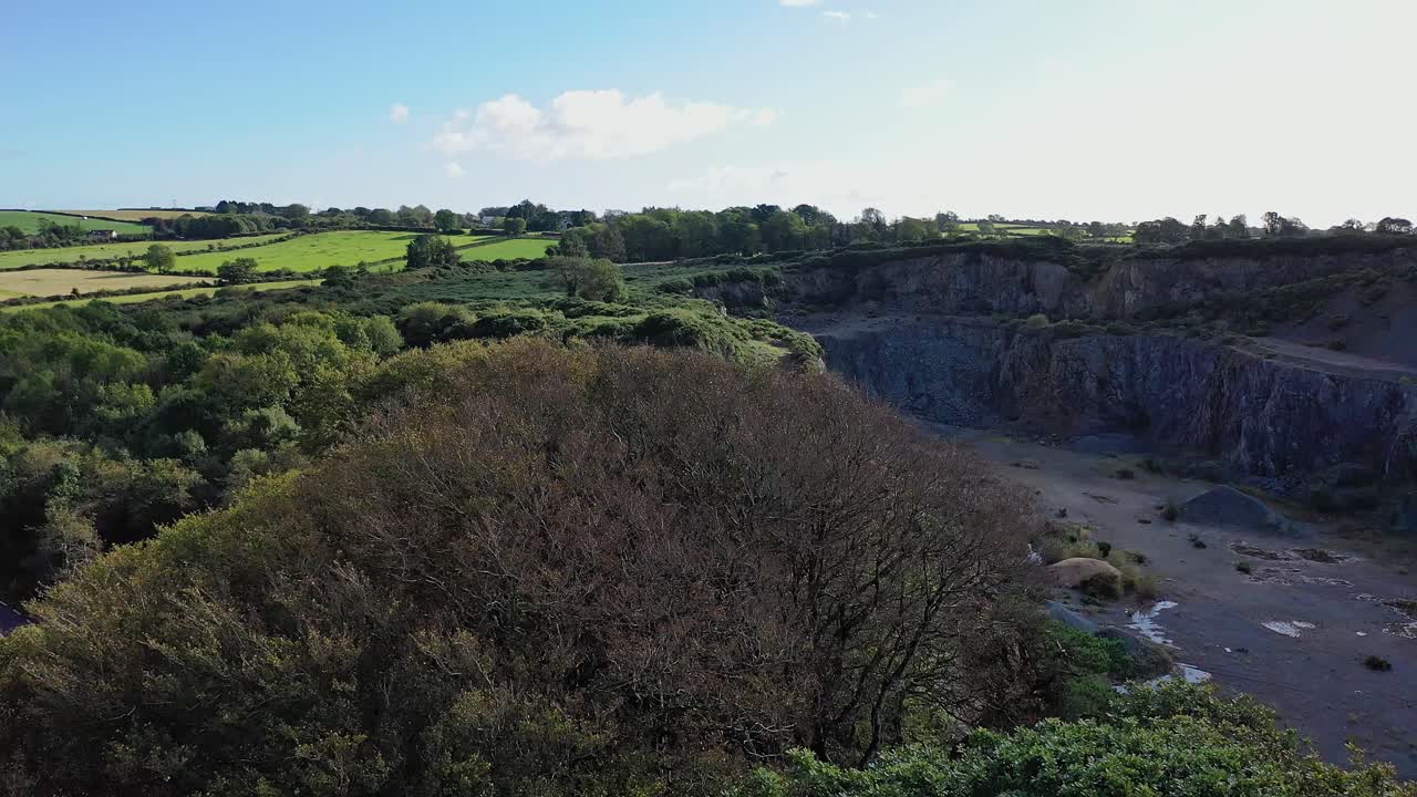 aerial view of tree tops to the side of abandoned quarry with blue sky and green fields in the distance
