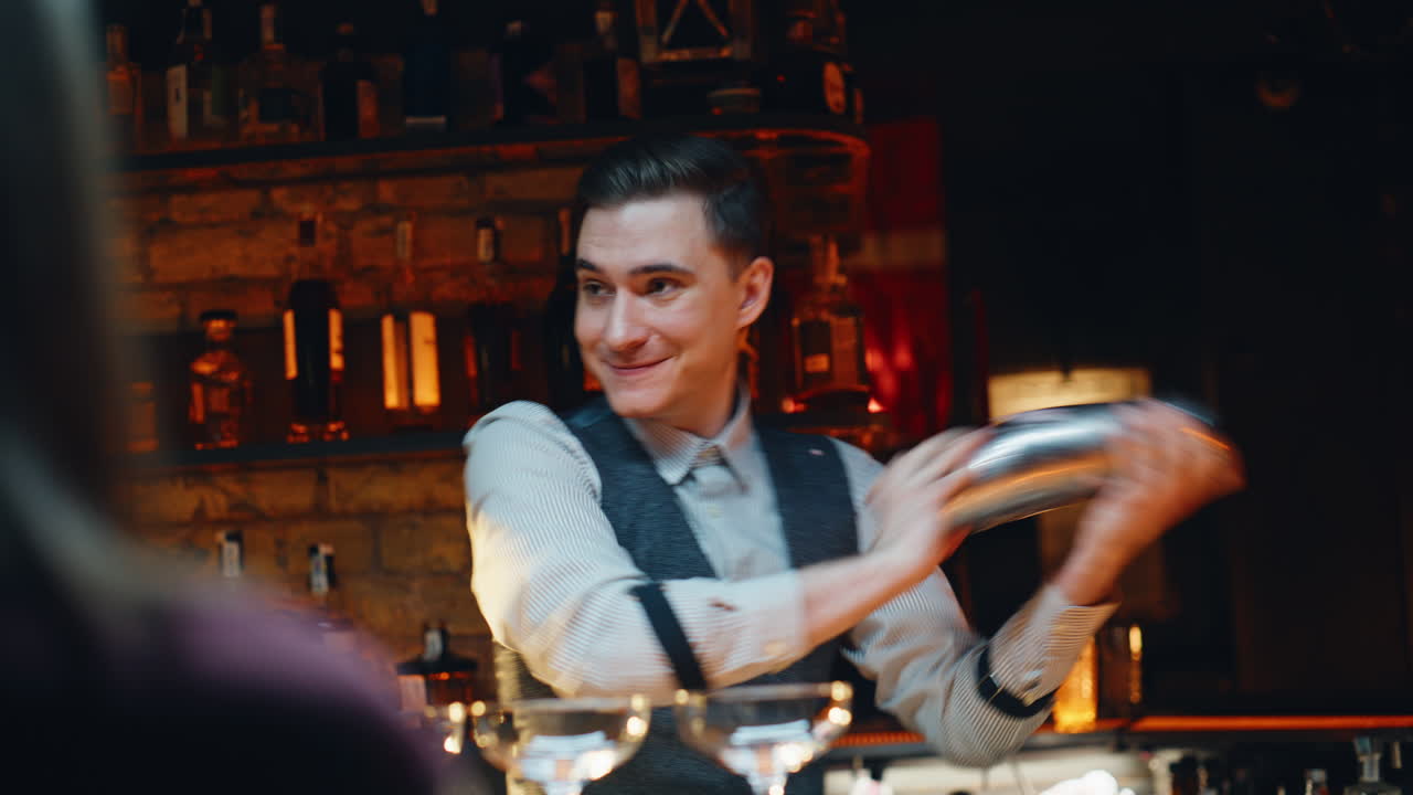Sorridente barista che prepara cocktail con lo shaker al bancone del bar. Barman che versa da bere