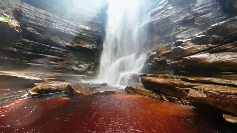 tilting up slow-motion action camera shot from the base of the mosquito waterfall surrounded by plants and cliffs and a river below in the chapada diamantina national park in northeastern brazil