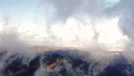 scenic view of rocky mountains through the clouds soaring high on a sunny day - aerial shot