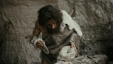 el hombre de las cavernas primitivo que usa piel de animal golpea la roca con una piedra afilada y hace una herramienta primitiva para cazar presas animales. el neandertal usando roca de sílex para crear la primera rueda. disparo en cámara lenta