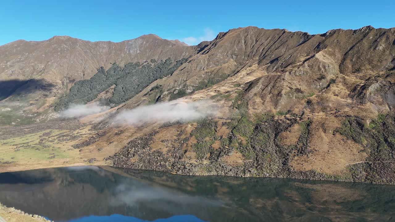 Aerial footage captures Lake Moke's serene landscape in Queenstown, New Zealand, with clear skies and rugged mountains