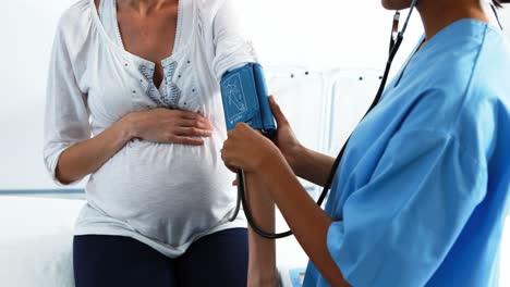 Mid-section-of-doctor-checking-blood-pressure-of-pregnant-woman