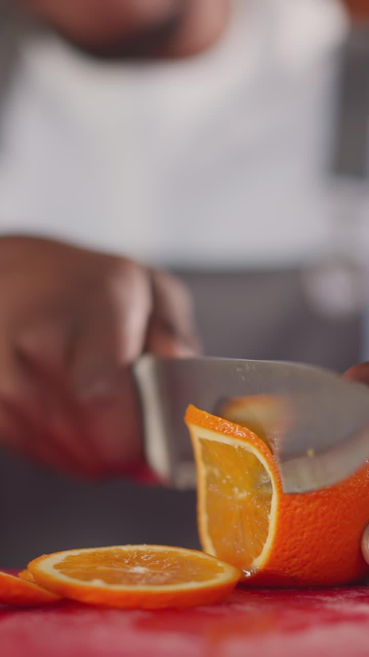 Barman cuts citrus on plastic board for cocktail closeup. Black servant prepares fresh beverage by cutting orange. African American bartender slices fruit