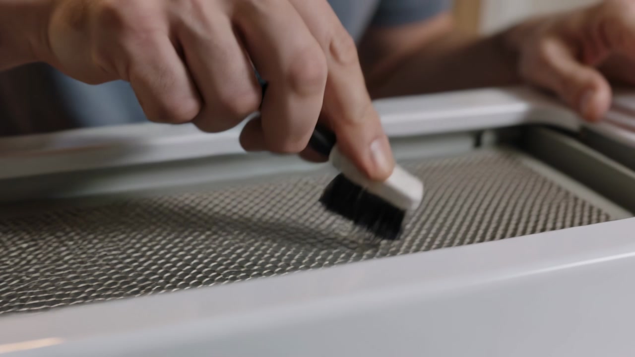Bringing brush, male in grey shirt cleaning mesh lint screen in laundry area for maintenance