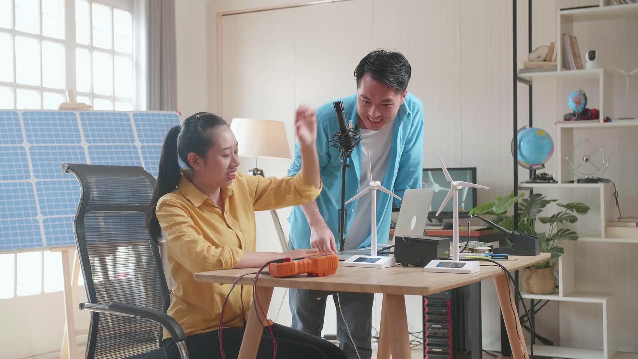 행복한 아시아 남녀가 사무실에서 태양전지 에 노트북으로 작업하는 동안 풍력 터빈을 성공적으로 테스트합니다.