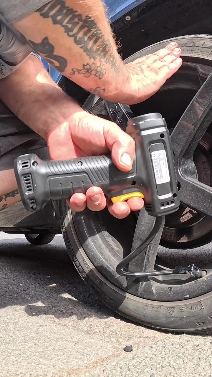 Vertical male holding cordless portable air pump to inflate van wheel and checking the pressure