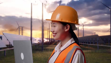 close up side view of asian female engineer with safety helmet working on a laptop and looking around with solar panel and wind turbines