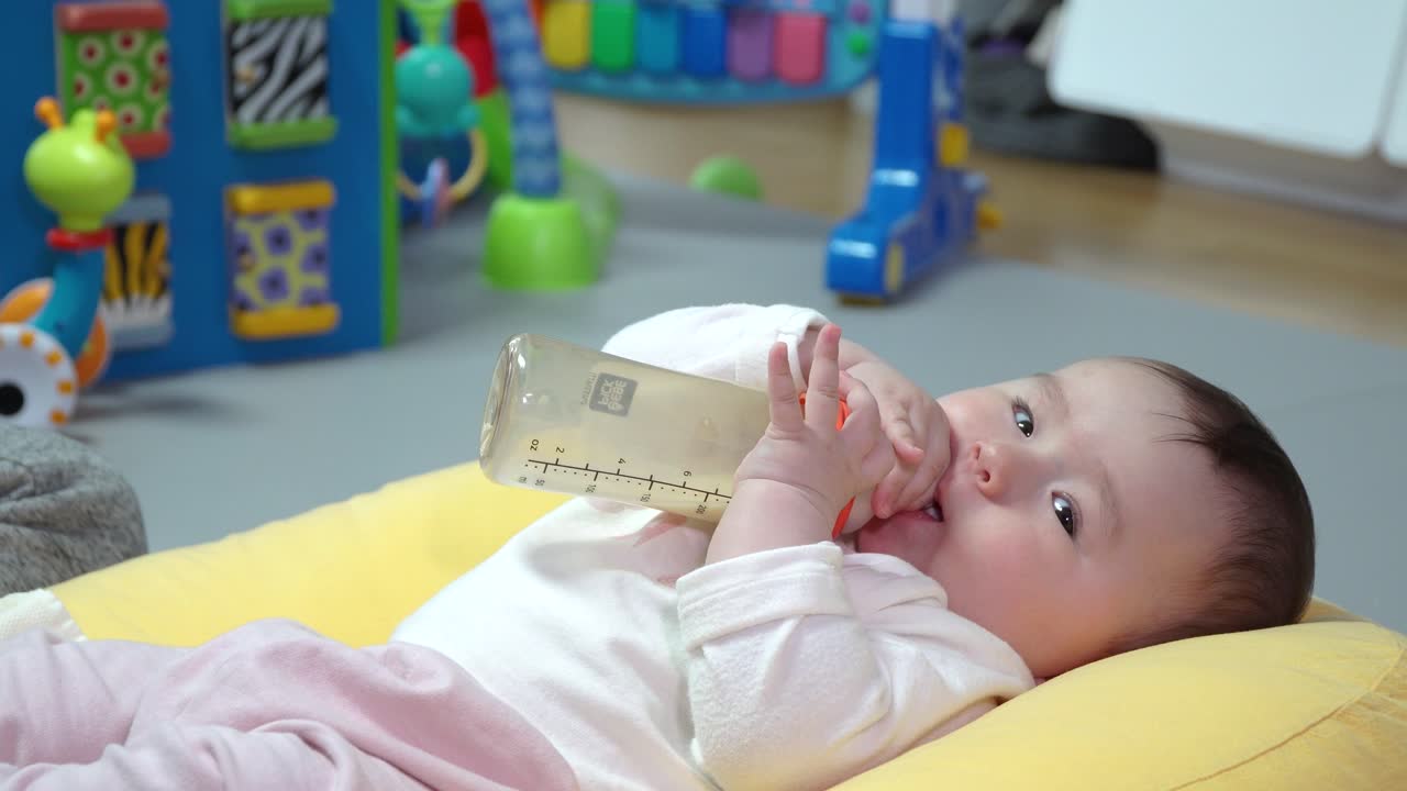 젖병을 들고 젖꼭지를 물고 누워있는 동안 노는 사랑스러운 아기