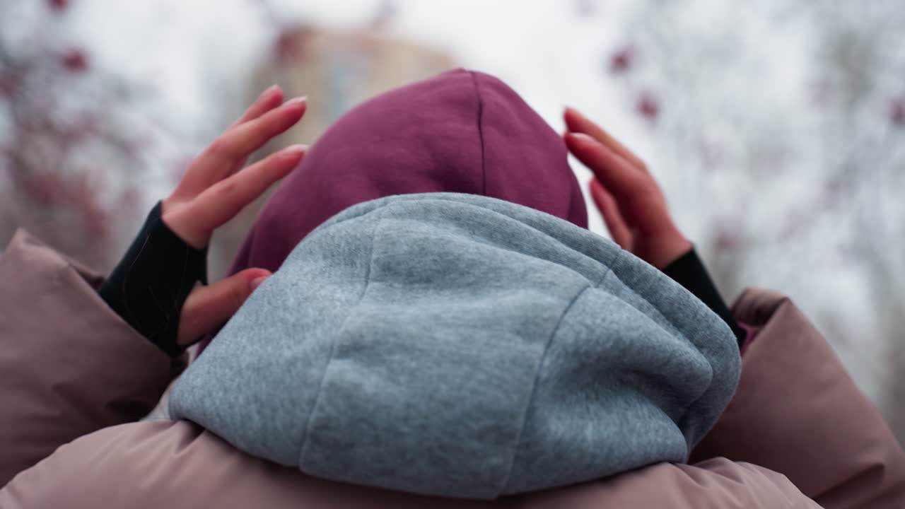 추운 겨울철에 는 동안 개별적으로 조정하는 베니의 근접 후면, 따뜻한 후디를 잡는 손, 나무와 건물의 흐릿한 배경