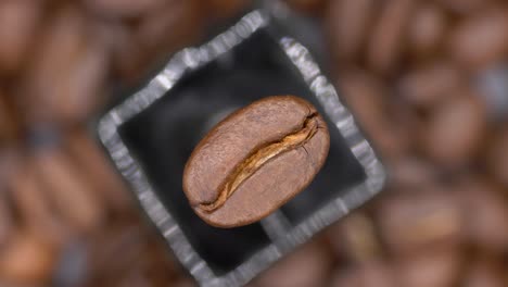 vista superior de un grano de café arábica asado que gira contra el fondo borroso de los granos de café