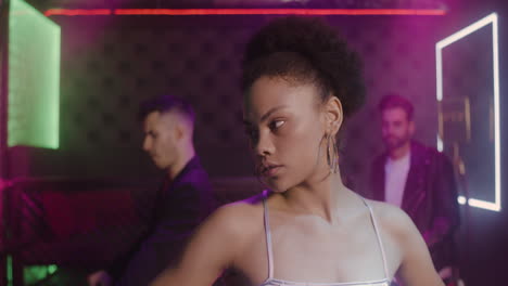 retrato de una chica hermosa que mira con confianza a la cámara en la discoteca mientras sus amigos bailan detrás de ella