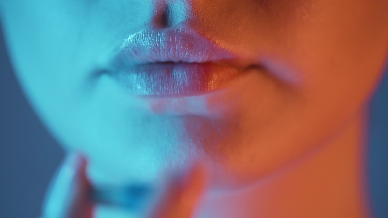 Extreme close up of a beautiful woman lip while she takes a capsule in nightlife to stay fit and fight nausea from alcohol for the evening in club in slow motion with blue and orange contrast in face