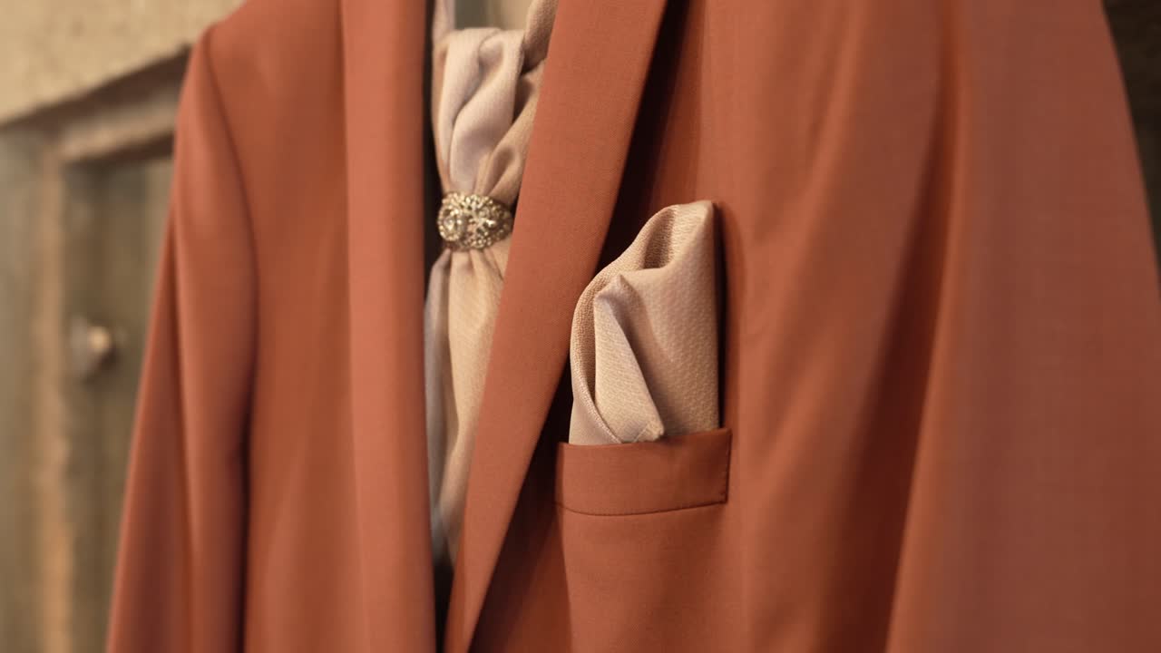 close up of refined brown suit with silk cravat adorned by jewel pin and folded pocket square