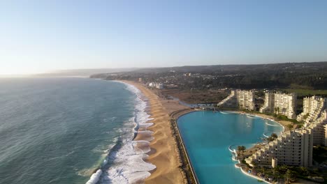 Volando-Sobre-Una-Enorme-Piscina-Junto-A-Edificios-Modernos-En-La-Playa-De-Algarrobo,-Chile