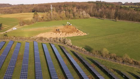 two large excavators driving around on a construction site behind a solar farm