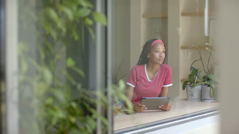 African-American-young-woman-holding-tablet,-looking-thoughtful