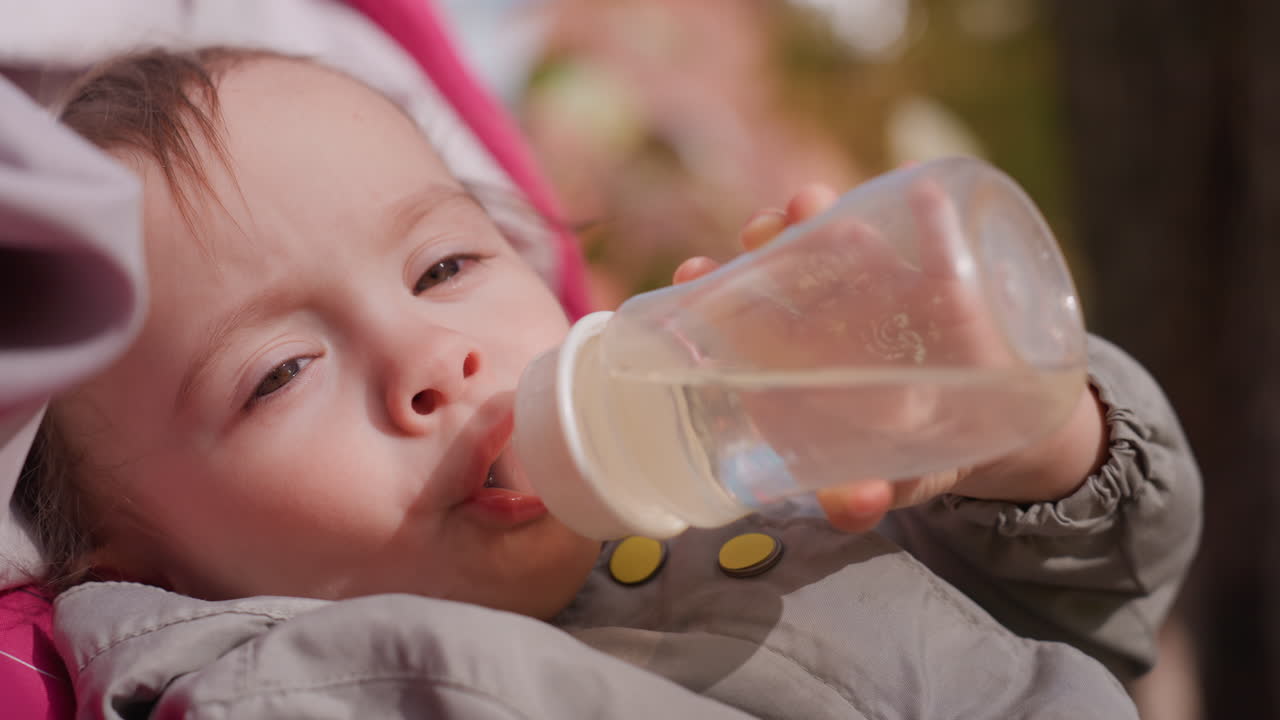 Bebê desfrutando da hora da alimentação durante passeio familiar ao ar livre no outono. Bebê adorável sendo nutrido com mamadeira enquanto sentado em carrinho em cena de parque de outono com guardião atencioso.
