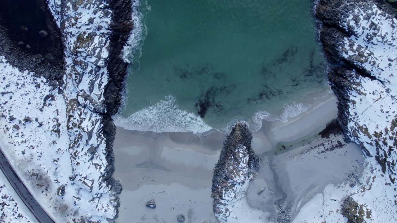 Veduta aerea a volo d'uccello della spiaggia di Andoya, Norvegia, con un bellissimo contrasto tra le rocce coperte di neve, il mare verde e le onde