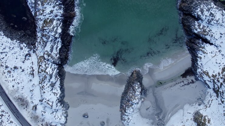 Veduta aerea a volo d'uccello della spiaggia di Andoya, Norvegia, con un bellissimo contrasto tra le rocce coperte di neve, il mare verde e le onde