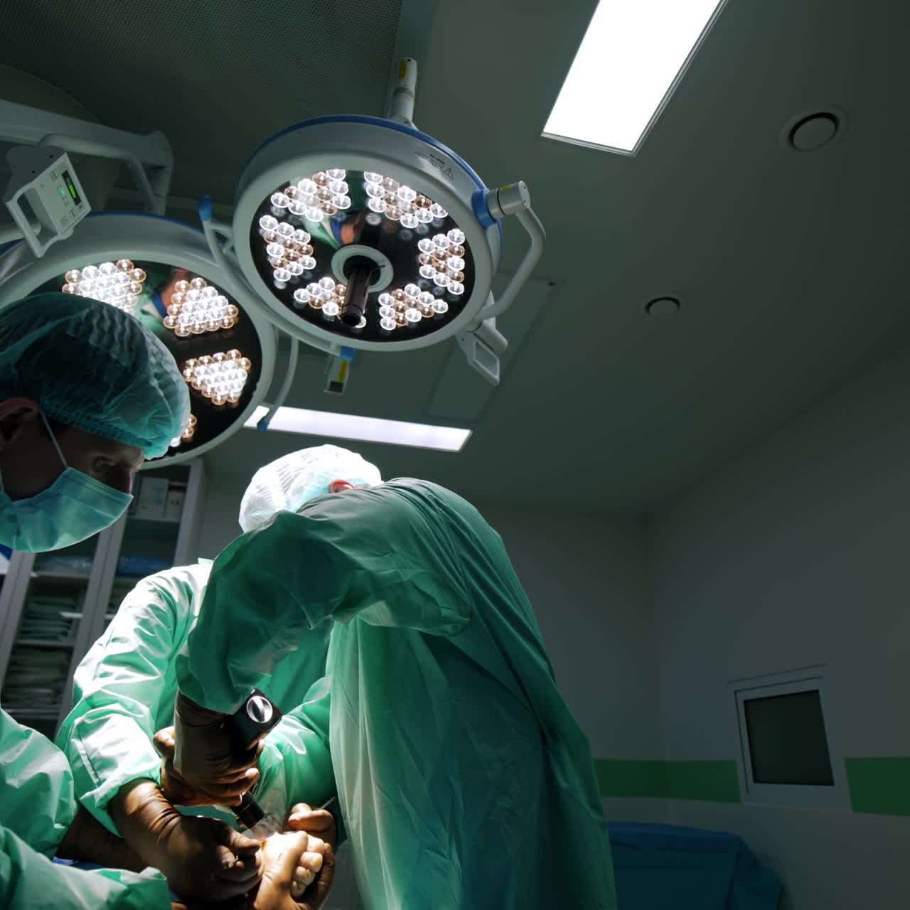 Chief surgeon uses medical surgical device in operation. Assistants hold the operated foot to help the surgeon