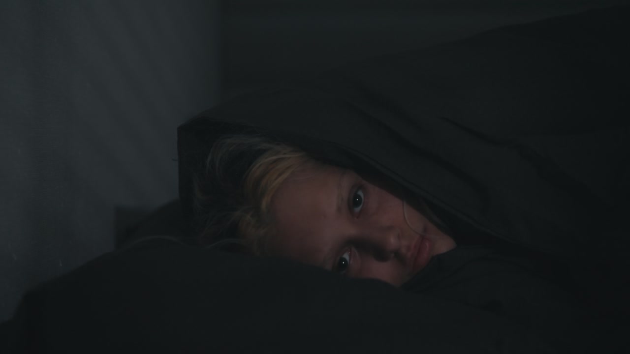 Portrait of a blonde girl who sharply falls her head in bed and covers herself with a gray blanket at night