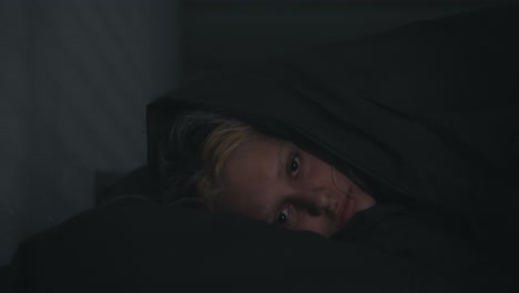 Portrait-of-a-blonde-girl-who-sharply-falls-her-head-in-bed-and-covers-herself-with-a-gray-blanket-at-night