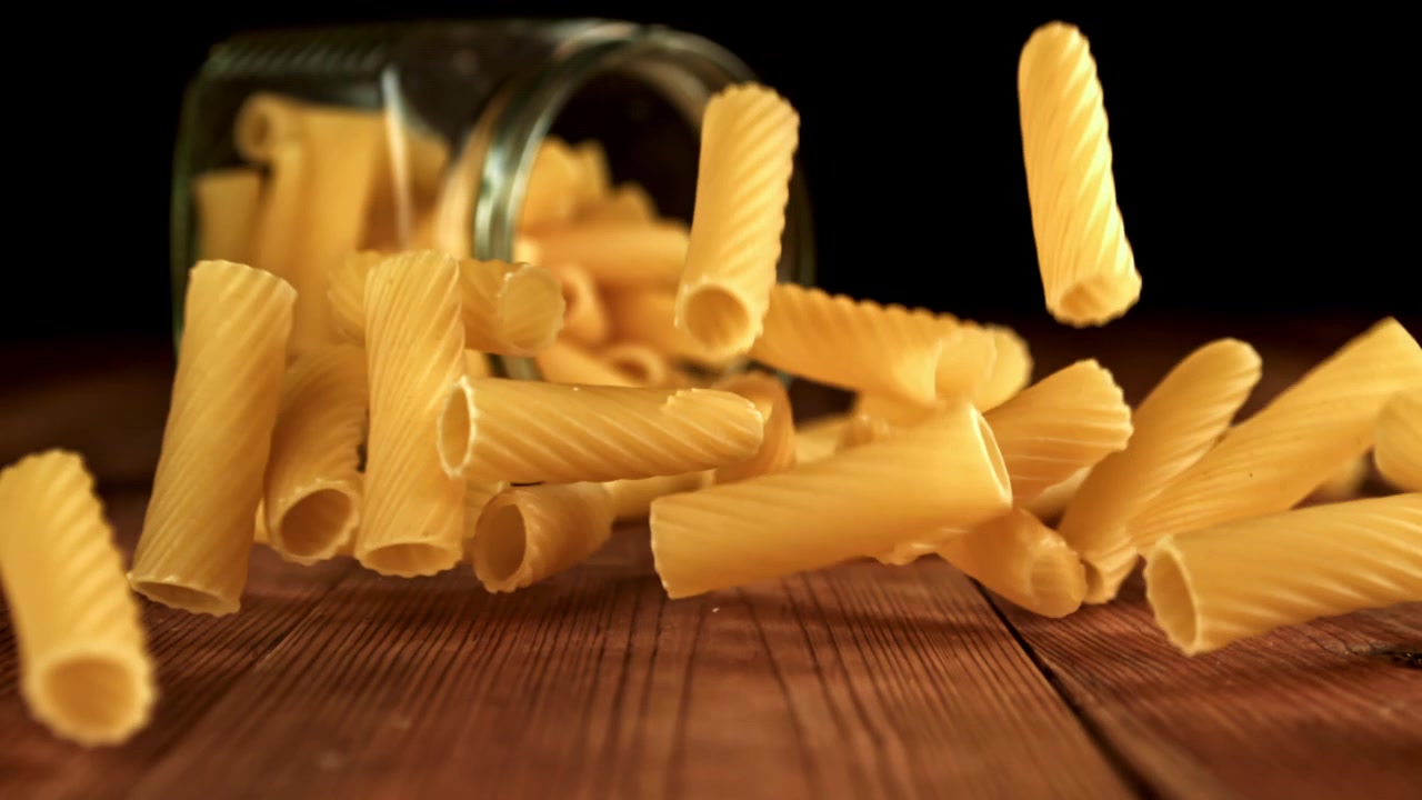 Pasta secca in caduta al rallentatore da un barattolo su un tavolo di legno