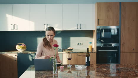 mujer de negocios viendo una computadora portátil en una cocina de lujo. mujer triste bebiendo vino tinto.
