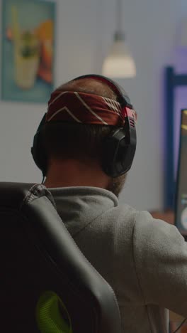 rear view of a gamer wearing headphones and a headband, sitting at a desk
