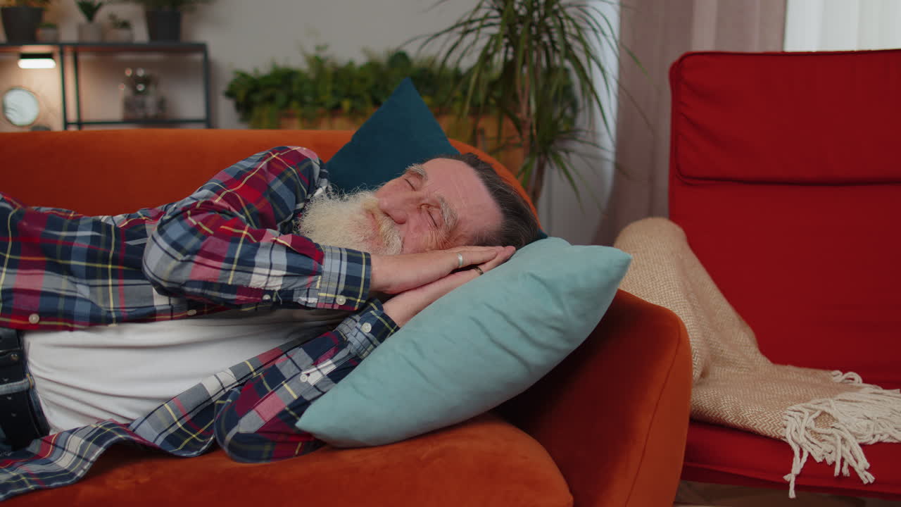 피곤한 한 노인이 침대에 누워서 집에서 휴식을 취하고, 잠을 자고, 소파에서 잠들고 있습니다.