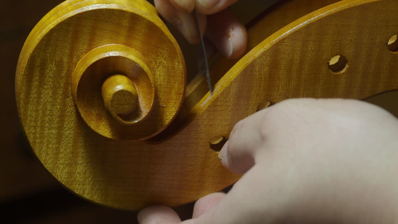 Skilled luthier carefully shaping wooden scroll of cello, demonstrating intricate craftsmanship with specialized hand tools and meticulous woodworking technique