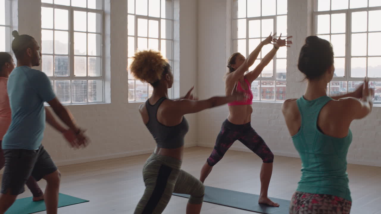 beautiful yoga class instructor teaching young group practicing warrior pose enjoying healthy lifestyle exercising in studio at sunrise