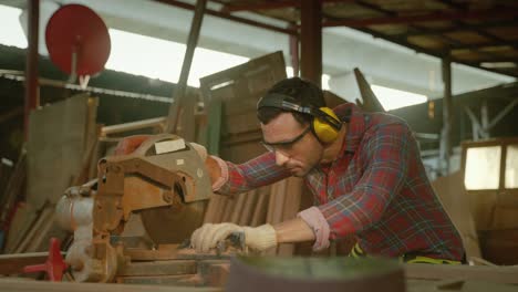 carpenter is using an electric circular saw to cut the wood to create the workpiece inside the wooden warehouse