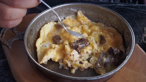 persona comiendo un plato de huevo revuelto de estilo turco con relleno de carne