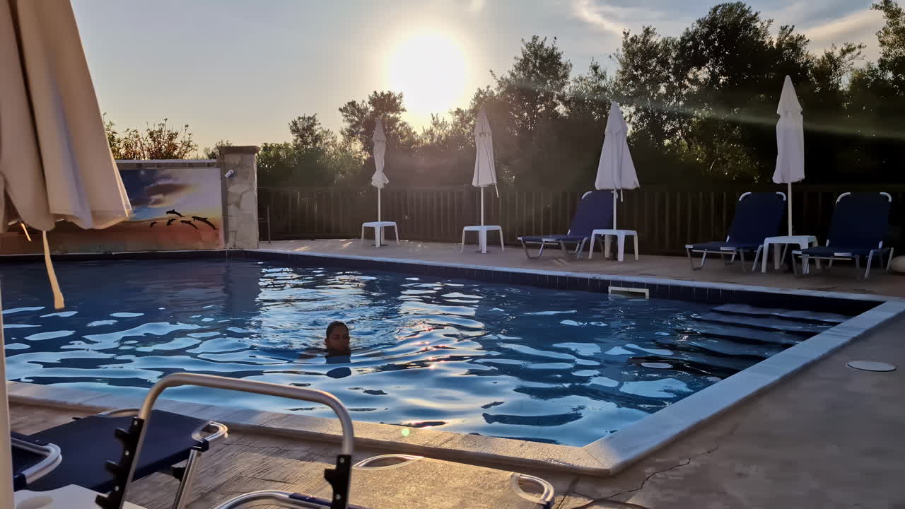 Frau schwimmt im Pool eines griechischen Resorts bei goldenem Sonnenlicht