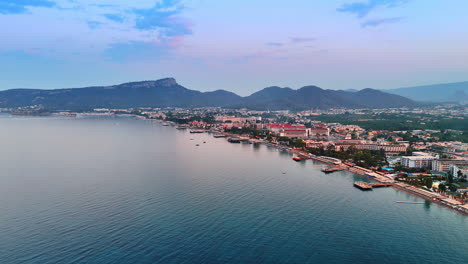 scenic coastal view of a seaside resort. scenic view of a coastal resort at sunset, showing lush mountains and a calm sea filled with boats and soft hues