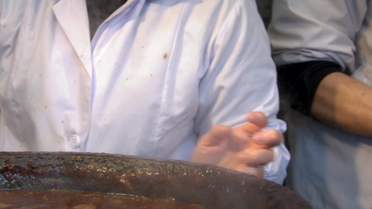 Uno chef in uniforme bianca cucina il tradizionale stufato di miso giapponese in una grande pentola fumante.