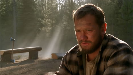 man in plaid shirt looking distressed in a forest setting with an axe