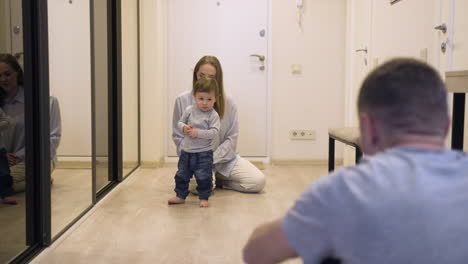 mother and her baby at one end of the corridor at home while the father encouraging the baby to walk to the other end