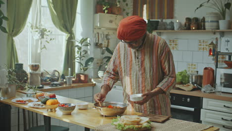 indian chef in turban serving freshly cooked meal in bowl and talking to camera